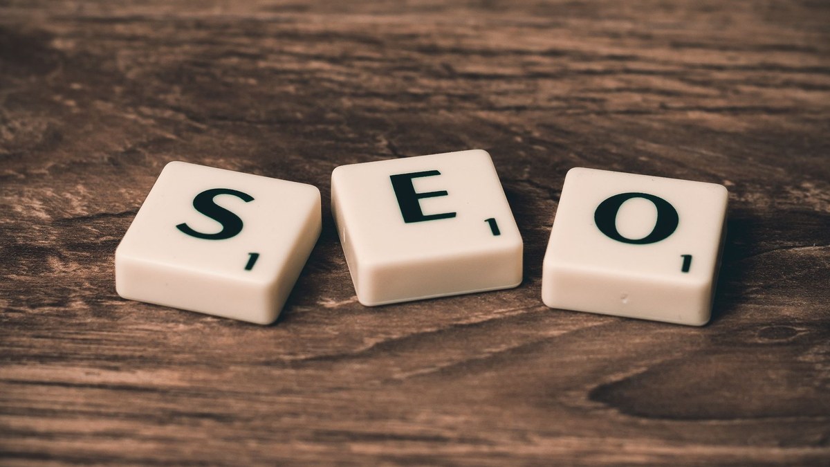 AI search visibility — Three white letter tiles spelling out SEO on a dark, textured wooden background.